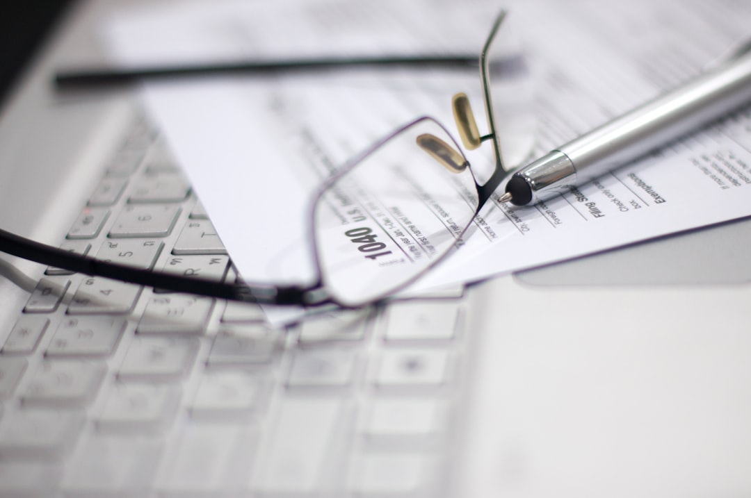 Tax Season: Horizontal side view of an office laptop, eyeglasses with a metallic pen on an Income Tax Return Form as a reminder, digitally generated image copy space